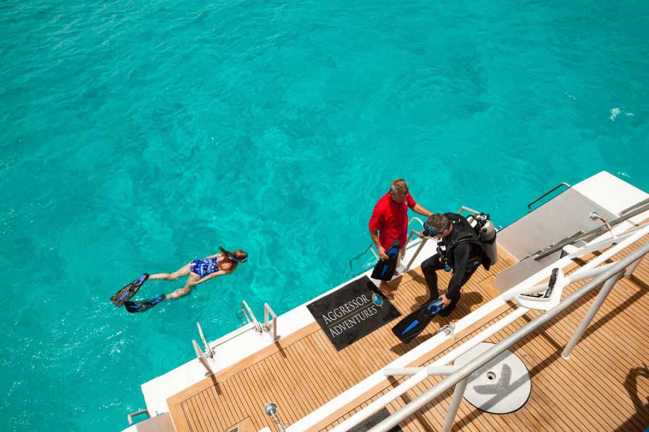 a scuba diver puts his fins on the boat while a snorkeler swims by in the ocean