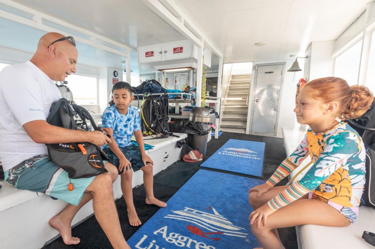 Two children onboard a yacht with an adult showing them scuba diving gear