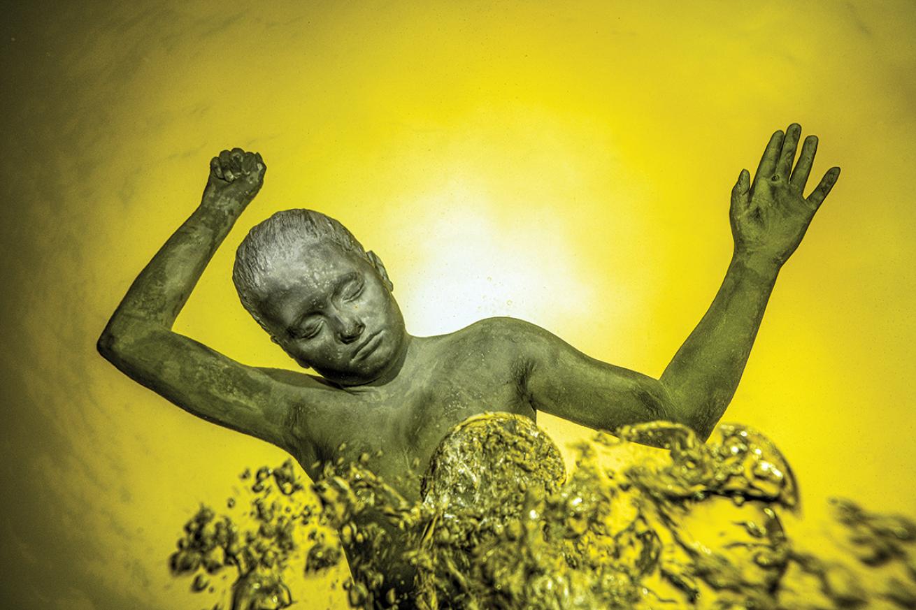 The statue of a young boy floats in water tinged yellow.