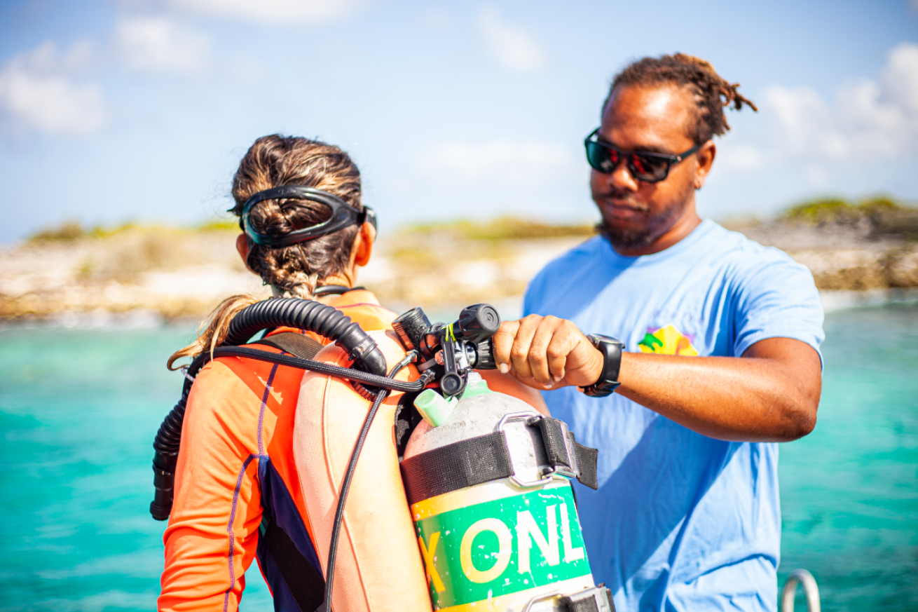 A person helping another person with their scuba tank