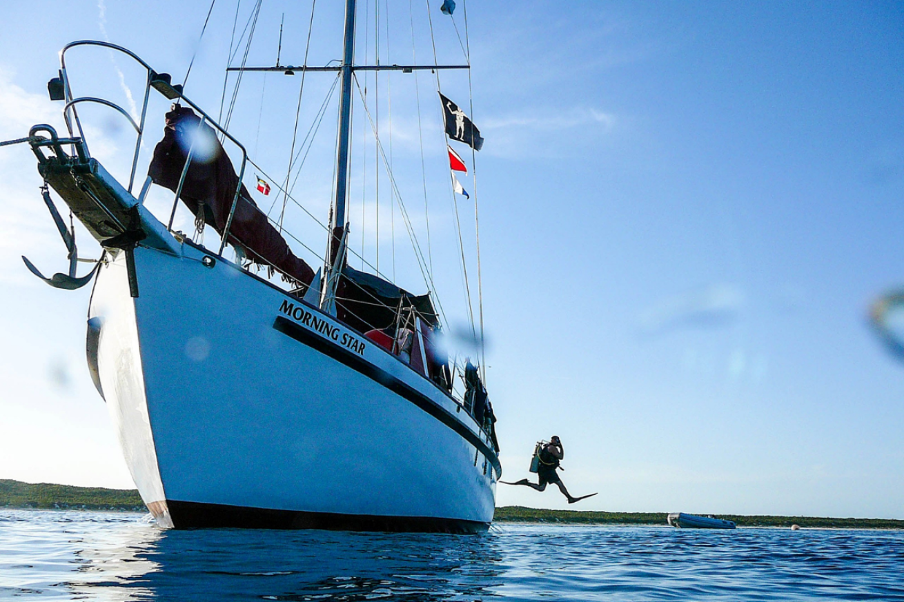 A sailboat with a person in scuba gear jumping off it