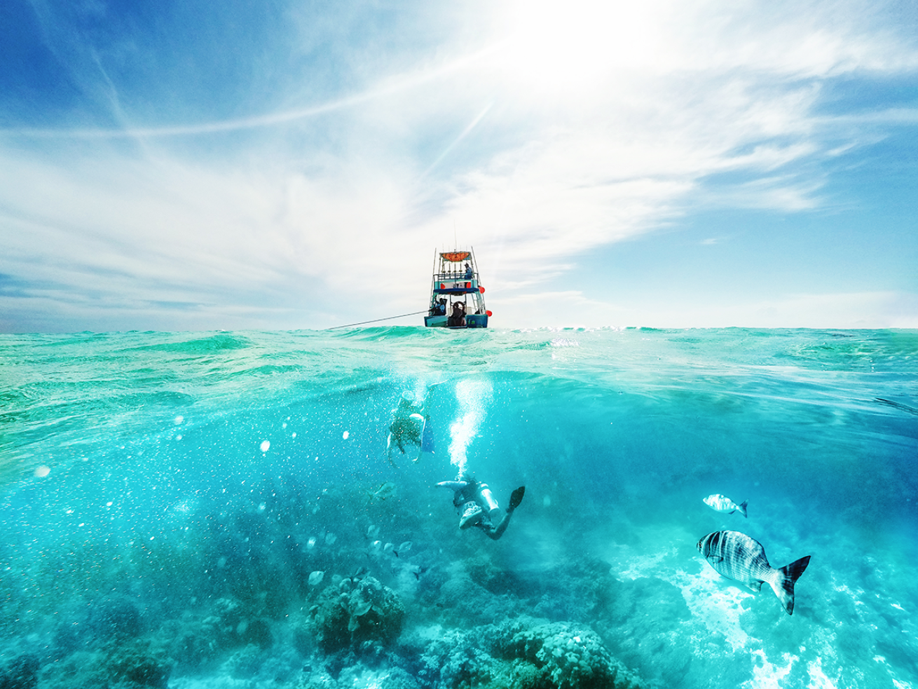 Boat in the middle of the ocean with fish swimming behind it.