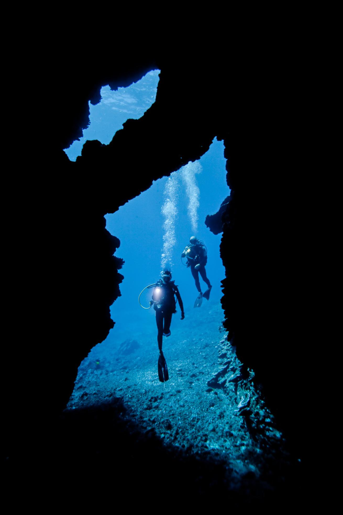 A pair of divers illuminates the entrance of First Cathedral, Hawaii