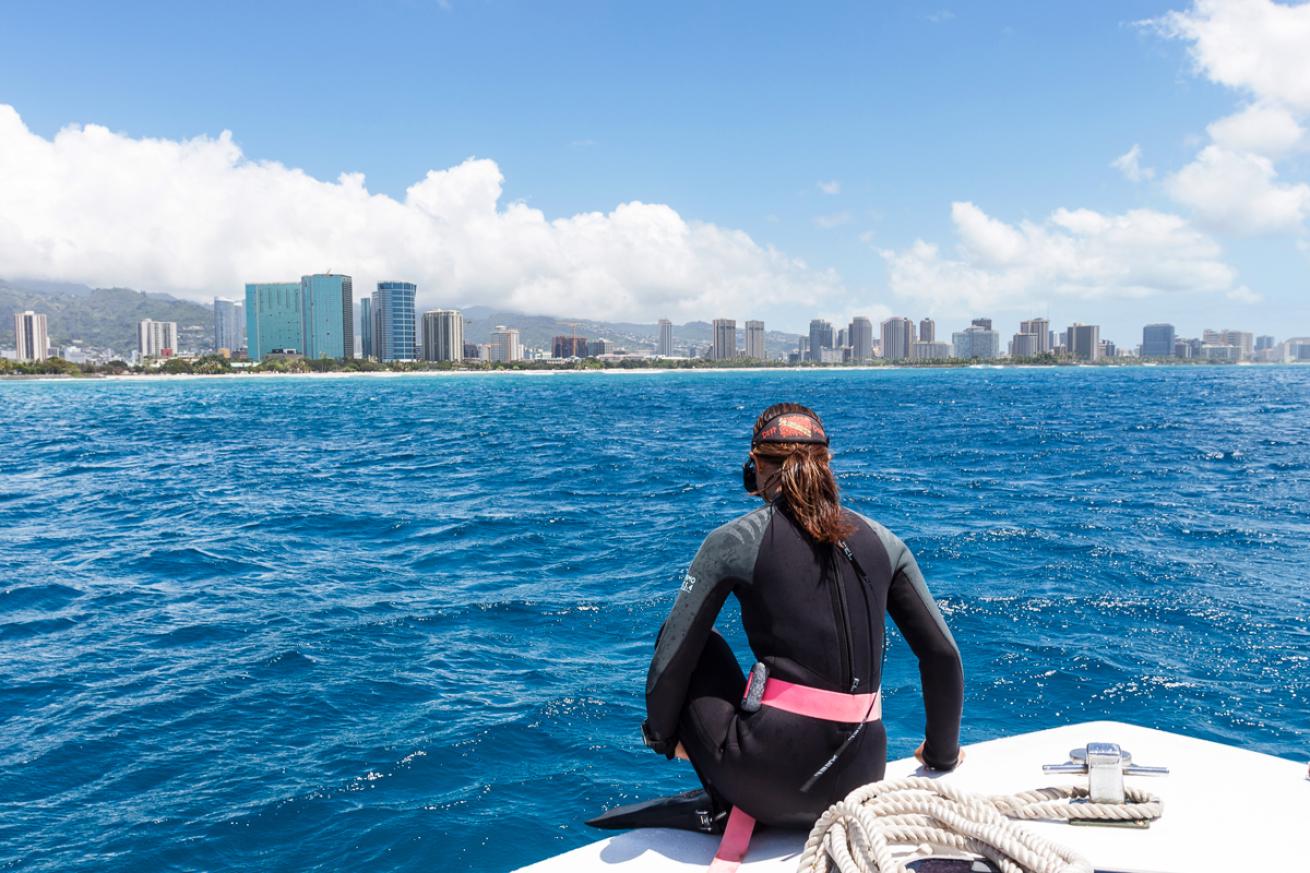 Woman in freediving gear sits at the bow of a boat about to dive in