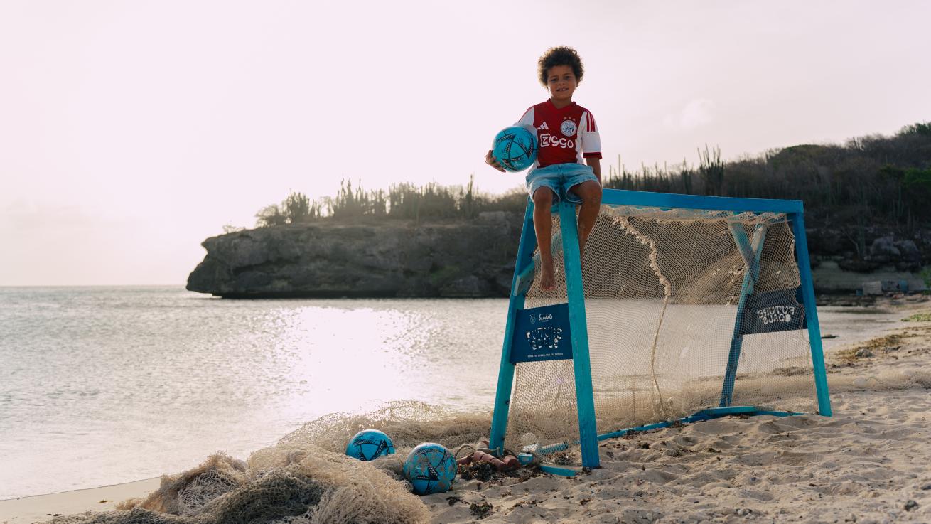 A child sitting on a goal with a football ball on the beach