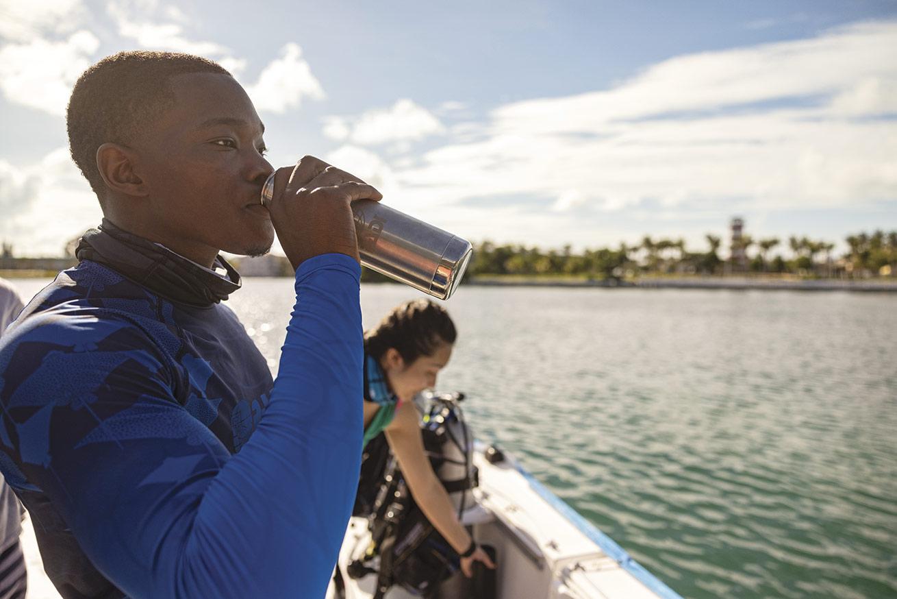 a diver drinks out of a reusable water bottle on a dive boat
