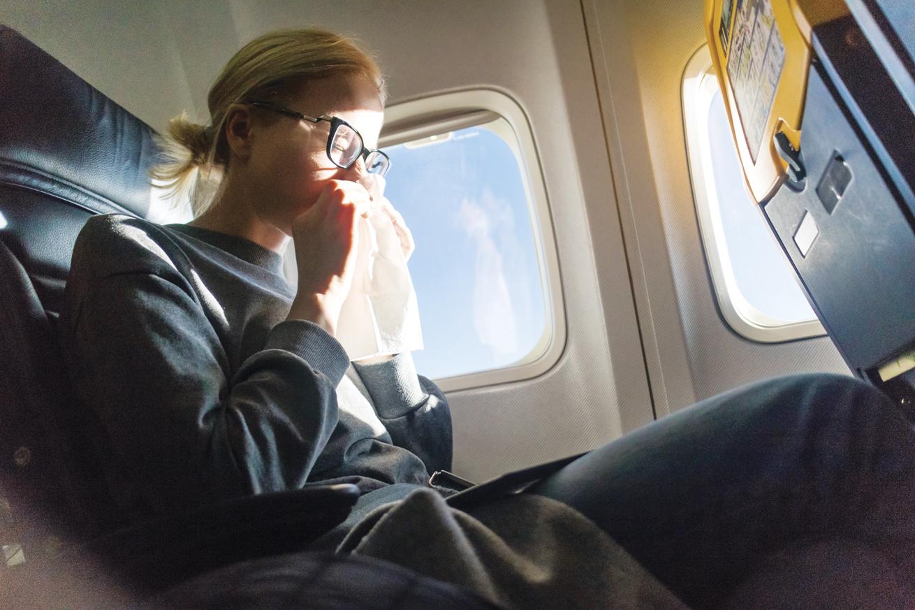 a woman on a plane with a tissue held up to her nose