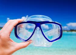 Scuba mask held in air with ocean in the background.